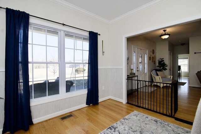 entryway featuring visible vents, baseboards, a wainscoted wall, ornamental molding, and wood finished floors