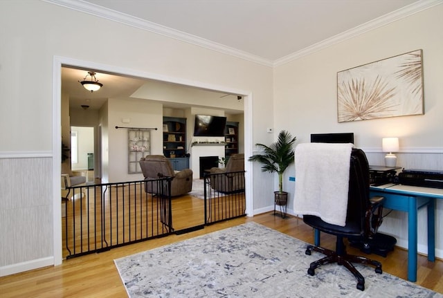 home office with a wainscoted wall, wood finished floors, a fireplace, and ornamental molding