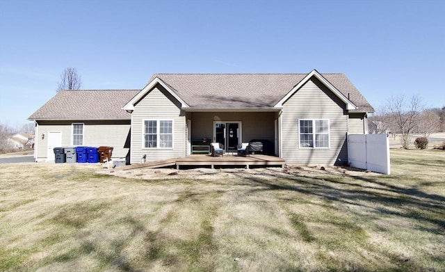 rear view of house featuring a deck, a yard, and roof with shingles