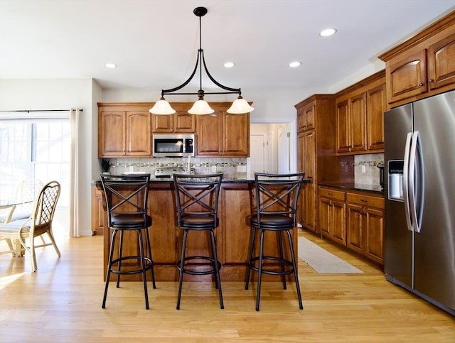 kitchen featuring a kitchen breakfast bar, backsplash, appliances with stainless steel finishes, and light wood-style floors