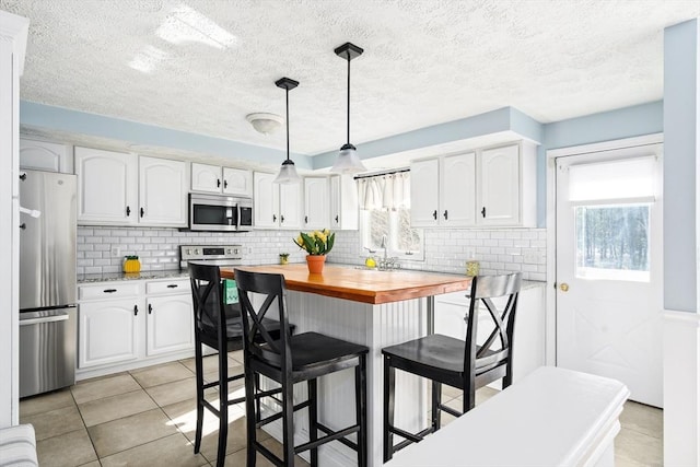 kitchen with appliances with stainless steel finishes, butcher block counters, hanging light fixtures, white cabinets, and a kitchen island