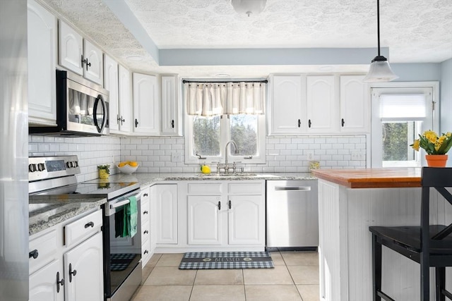 kitchen featuring sink, light stone counters, appliances with stainless steel finishes, pendant lighting, and white cabinets