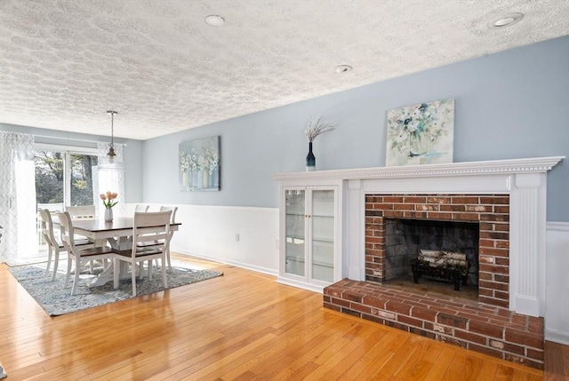 dining room with a brick fireplace, wood-type flooring, and a textured ceiling