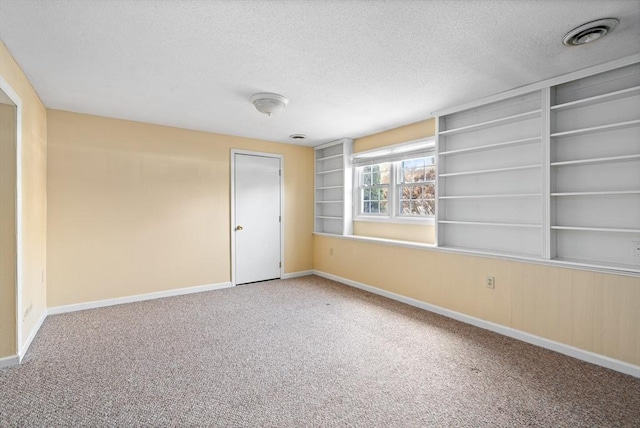 carpeted spare room featuring built in shelves and a textured ceiling