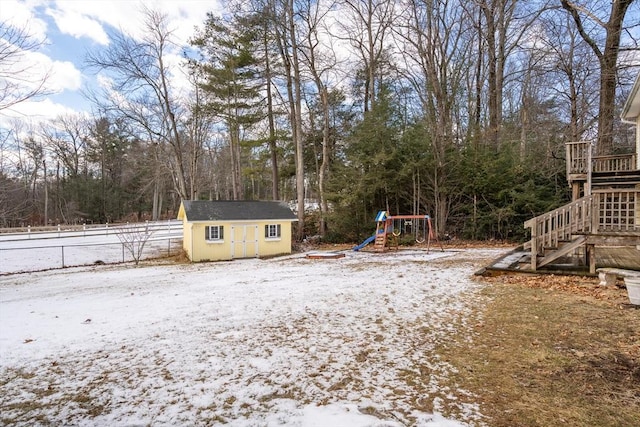 snowy yard featuring a playground and a storage unit