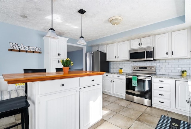 kitchen with tasteful backsplash, white cabinetry, hanging light fixtures, light tile patterned floors, and stainless steel appliances