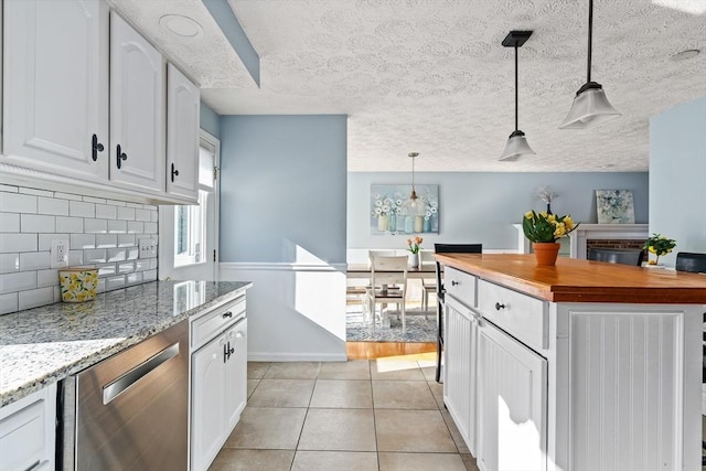 kitchen featuring decorative light fixtures, light tile patterned floors, stainless steel dishwasher, light stone countertops, and white cabinets