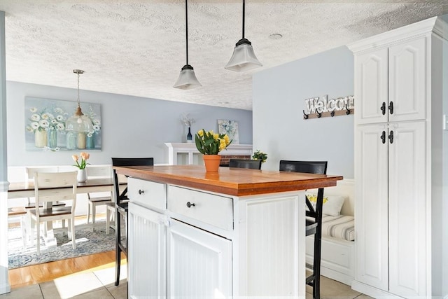 kitchen with butcher block counters, white cabinetry, a textured ceiling, a kitchen island, and pendant lighting