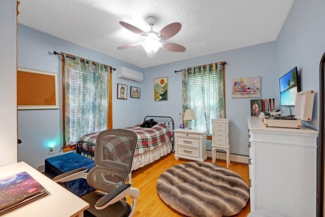 bedroom with baseboard heating, an AC wall unit, light wood-type flooring, and ceiling fan
