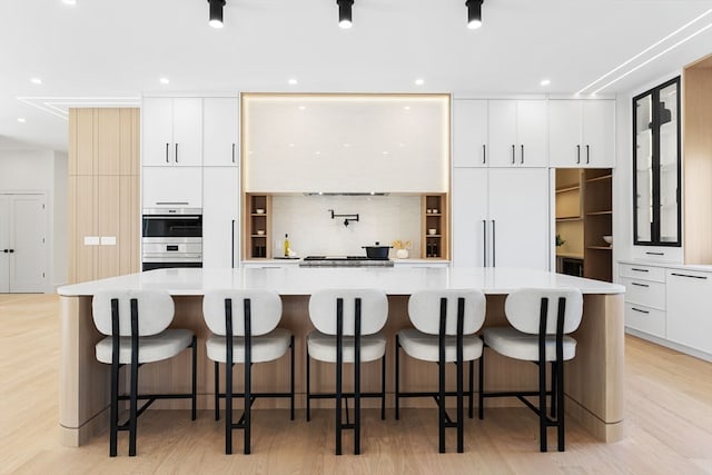 kitchen with light wood-type flooring, a breakfast bar, a large island, and double oven