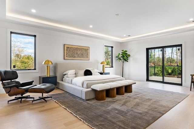 bedroom with a tray ceiling, light hardwood / wood-style flooring, and access to outside