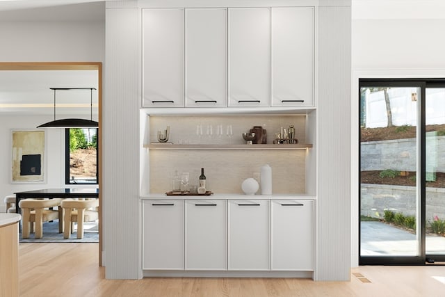 bar with white cabinets, light hardwood / wood-style floors, and pendant lighting