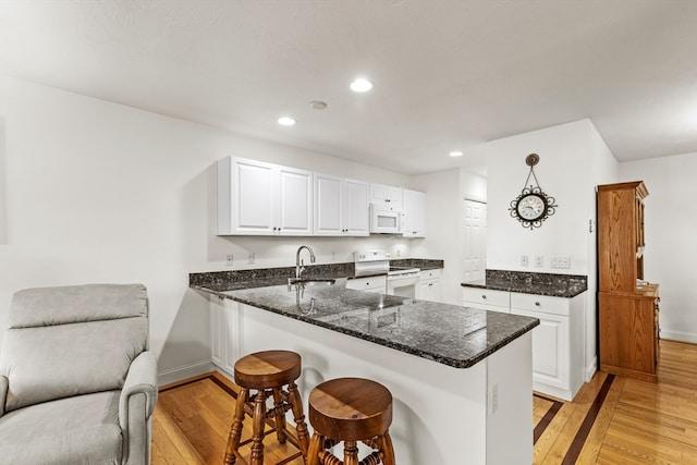 kitchen with white cabinetry, kitchen peninsula, white appliances, and light hardwood / wood-style floors