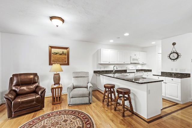 kitchen with white cabinets, a kitchen breakfast bar, light hardwood / wood-style flooring, and white appliances