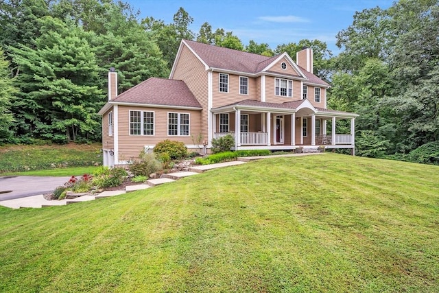 view of front facade with a chimney, covered porch, a front yard, and driveway