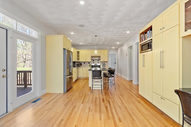 kitchen featuring stainless steel appliances, a breakfast bar, light wood-type flooring, glass insert cabinets, and recessed lighting