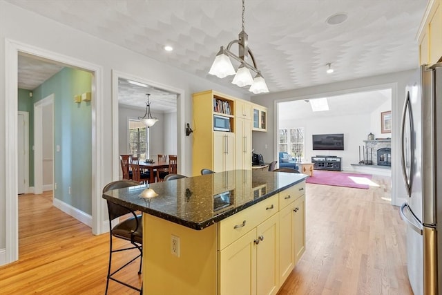 kitchen featuring freestanding refrigerator, light wood-type flooring, baseboards, open floor plan, and dark stone counters
