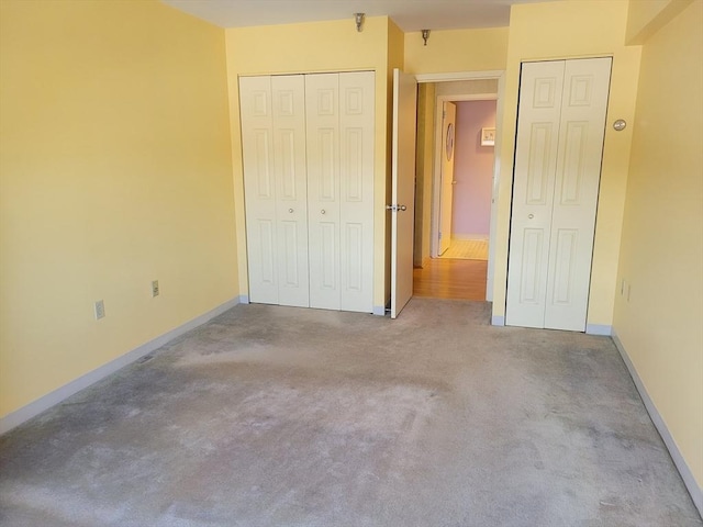 unfurnished bedroom featuring baseboards, carpet floors, and two closets