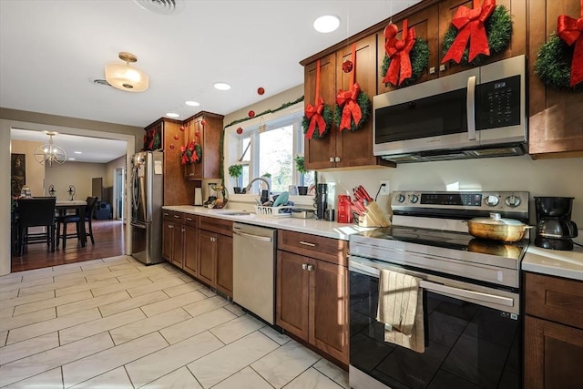 kitchen with sink, stainless steel appliances, hanging light fixtures, and an inviting chandelier