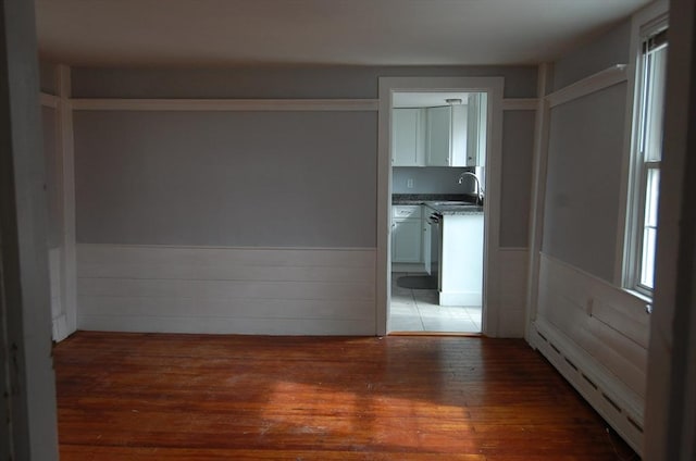 unfurnished room featuring a baseboard heating unit, a wainscoted wall, a sink, and wood finished floors