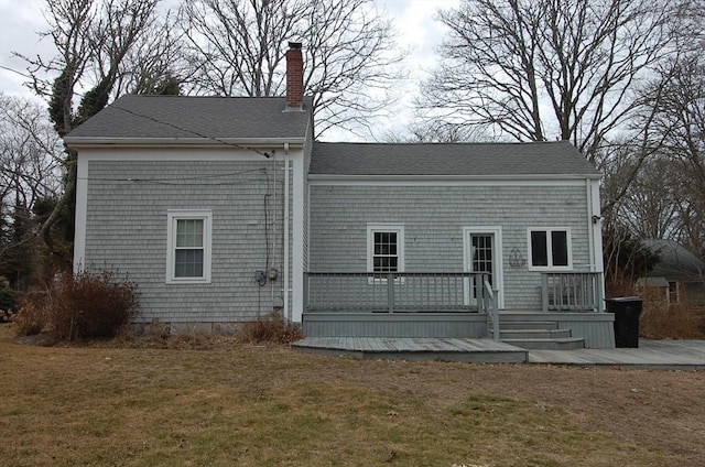 back of house featuring a shingled roof, a chimney, a deck, and a yard