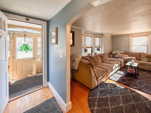 living room with light wood-type flooring, arched walkways, baseboards, and ornamental molding