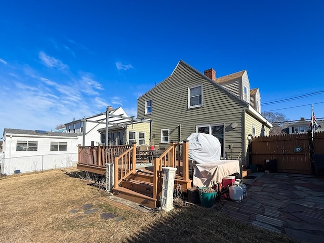 back of property with a wooden deck, a chimney, and fence