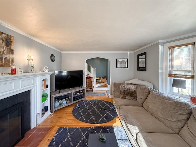 living room with a fireplace with flush hearth, ornamental molding, stairway, arched walkways, and light wood-style floors