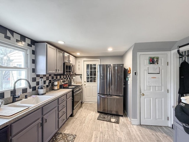 kitchen with gray cabinetry, light wood-style flooring, a sink, stainless steel appliances, and decorative backsplash