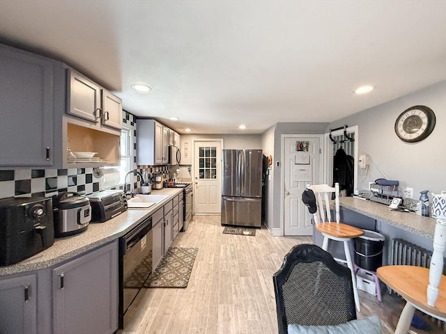 kitchen with light wood-type flooring, a sink, tasteful backsplash, appliances with stainless steel finishes, and light countertops