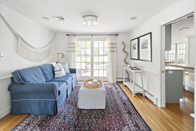 living area with light wood-type flooring, healthy amount of natural light, ornamental molding, a wainscoted wall, and a baseboard heating unit