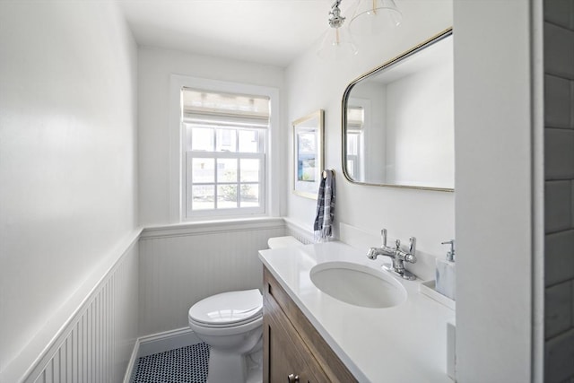half bathroom with a wainscoted wall, toilet, vanity, and tile patterned flooring