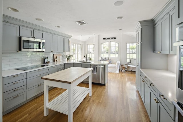 kitchen with stainless steel appliances, gray cabinetry, a peninsula, a sink, and recessed lighting