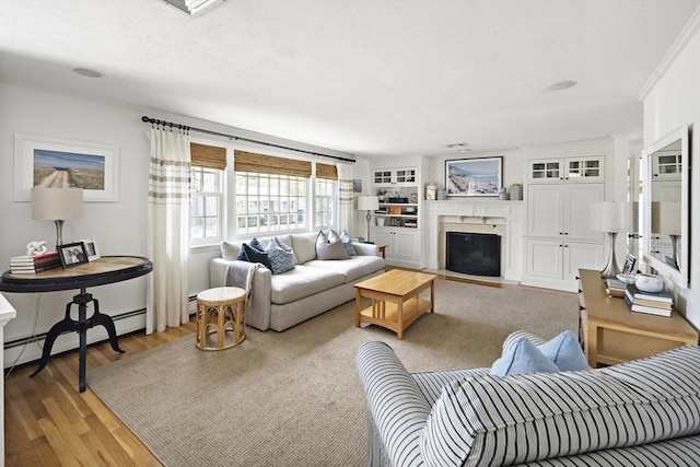 living room featuring a fireplace with flush hearth, wood finished floors, baseboard heating, and crown molding