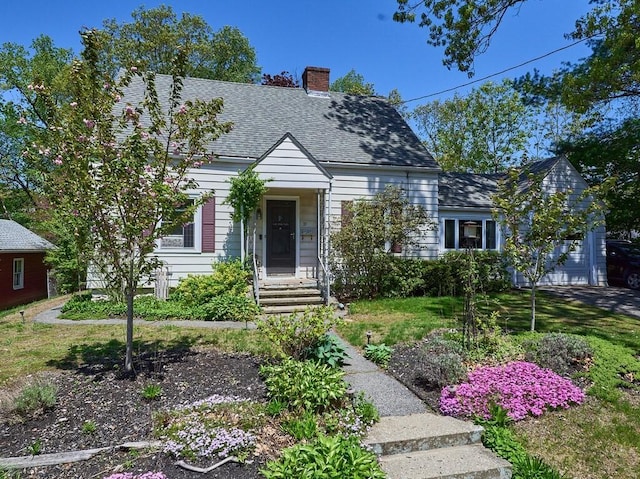 cape cod house featuring a chimney, a shingled roof, and a front lawn