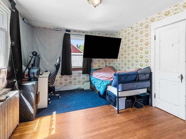 bedroom with wallpapered walls, radiator, and wood finished floors