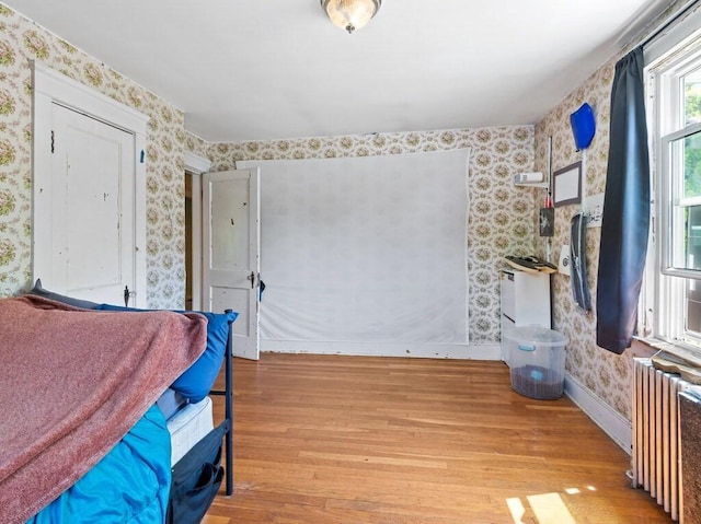 bedroom with radiator, wallpapered walls, wood finished floors, and baseboards