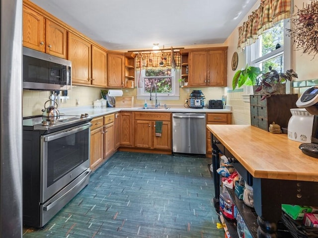 kitchen with appliances with stainless steel finishes, open shelves, a sink, light countertops, and plenty of natural light