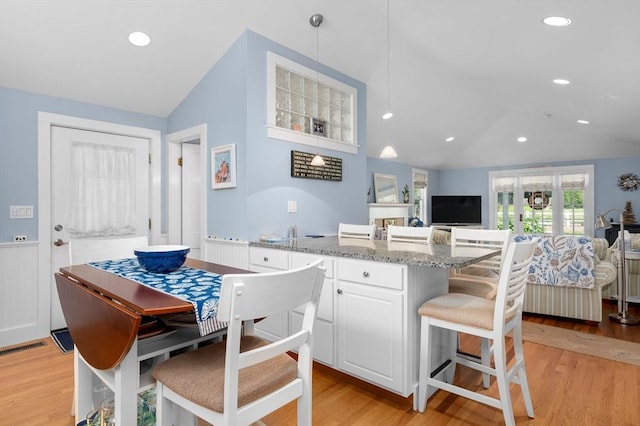 46 Pine, Falmouth, MA 02556 - kitchen featuring vaulted ceiling, light stone counters, light wood-style flooring, white cabinets, and wainscoting