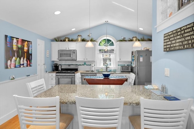 46 Pine, Falmouth, MA 02556 - kitchen with stainless steel appliances, lofted ceiling, white cabinets, light stone countertops, and wainscoting