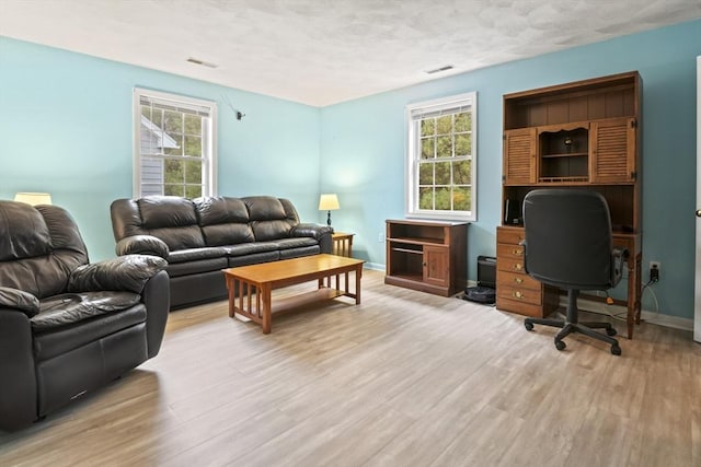 living area with light wood finished floors, baseboards, an office area, and a textured ceiling