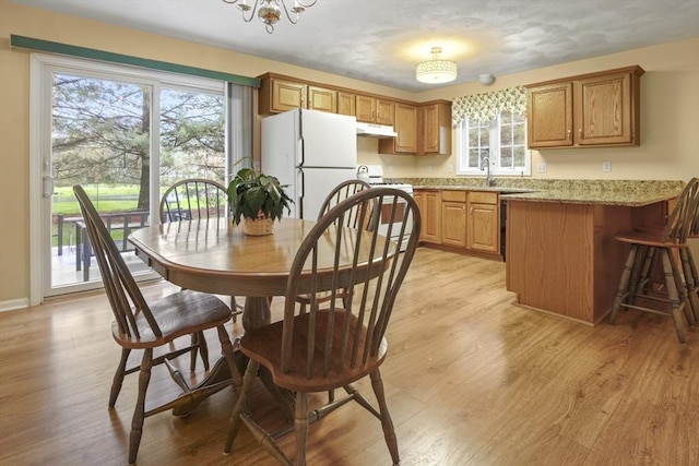 kitchen featuring under cabinet range hood, white appliances, a peninsula, light wood-style flooring, and brown cabinets