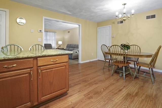 kitchen featuring light wood finished floors, brown cabinetry, a chandelier, light stone counters, and baseboards