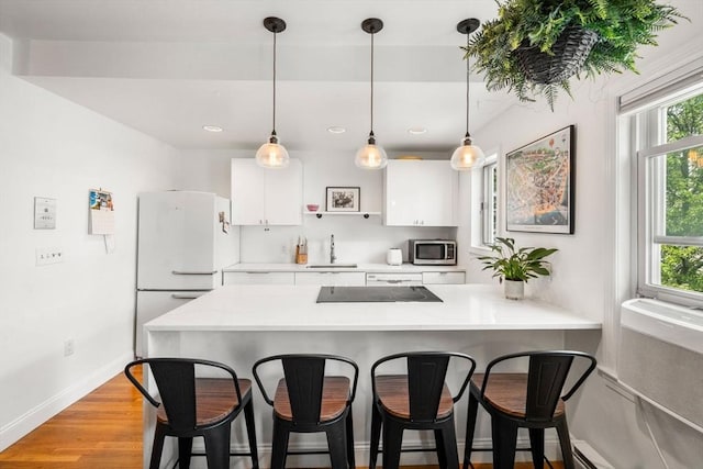 122 W 9th St Unit 2, Boston, MA 02127 - kitchen featuring stainless steel microwave, freestanding refrigerator, light countertops, white cabinetry, and a kitchen breakfast bar