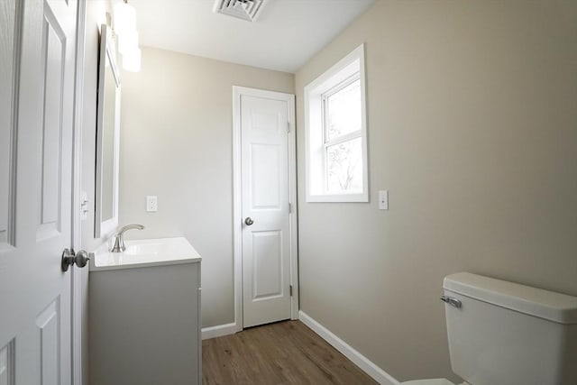 half bathroom with visible vents, baseboards, toilet, wood finished floors, and vanity