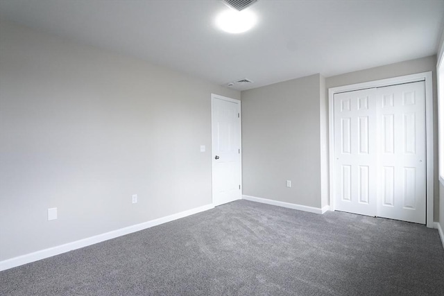 unfurnished bedroom with a closet, visible vents, dark carpet, and baseboards