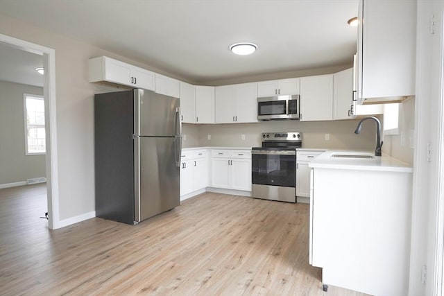 kitchen featuring light wood-style flooring, a sink, light countertops, appliances with stainless steel finishes, and white cabinetry