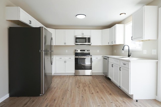 kitchen featuring light wood-style flooring, a sink, light countertops, white cabinets, and appliances with stainless steel finishes