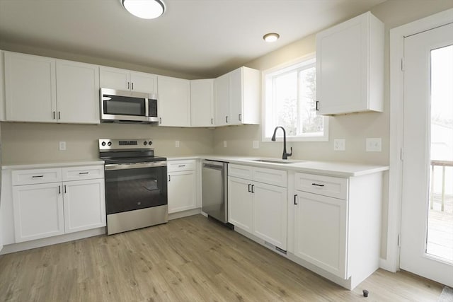 kitchen featuring a sink, stainless steel appliances, light countertops, light wood-style floors, and white cabinetry