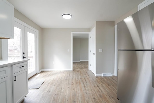 kitchen with visible vents, light wood-style flooring, light countertops, and freestanding refrigerator